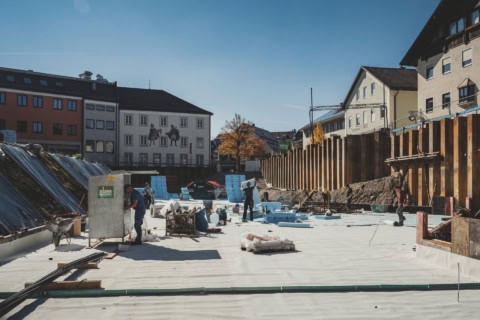 Roof construction workers installing underlayment with a cityscape background, showcasing skilled labor on a building project with residential and commercial structures.