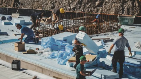Heavy construction workers installing insulation on a building roof, with rebar fixtures in background, showcasing commercial roof insulation and waterproofing process.