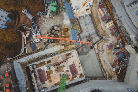 Crane lifting concrete for building construction site, aerial view of early-stage commercial building foundation work, construction progress in urban development.