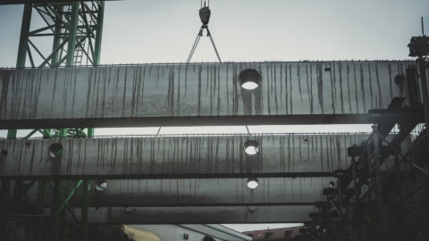 Corrosion-stained concrete beams at a construction site, showcasing for structural support and safety; industrial scaffolding and equipment visible in the background.