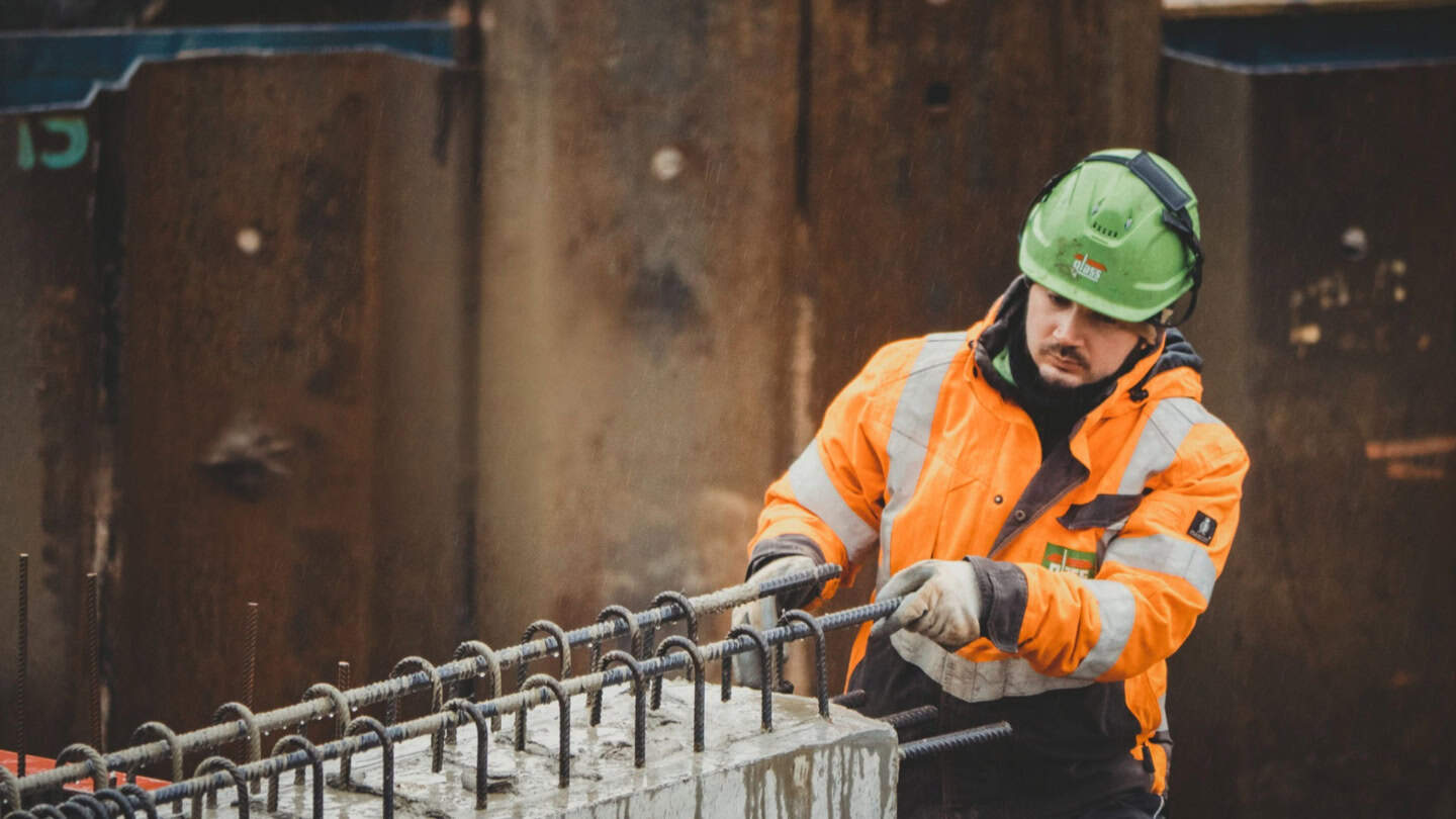 Rebar installation for construction site concrete pouring, construction worker in safety gear, https://mpgbau.de, focused on improve construction safety and concrete reinforcement.