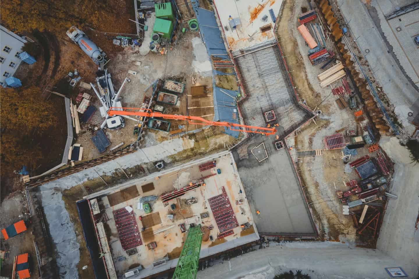 Aerial view of a construction site with a crane, concrete foundations, and building materials, showcasing active building progress and infrastructure development.