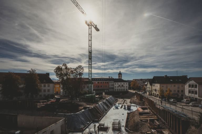 Construction site with a tower crane and partially built infrastructure in a residential area under a cloudy sky, showcasing modern urban development and structural staging processes.