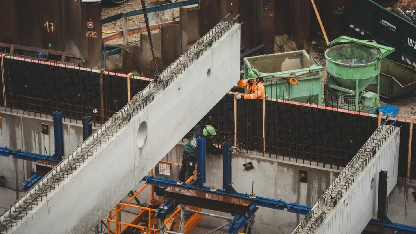Welding workers assembling concrete structures at a construction site with safety gear and reinforcement bars.
