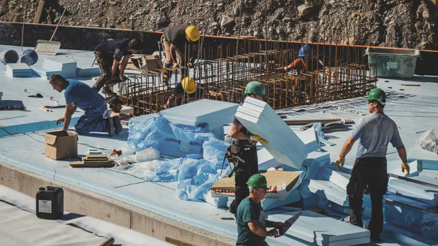 Reinforced concrete construction workers at a building site, installing insulation and preparing rebar framework for the next phase of building.